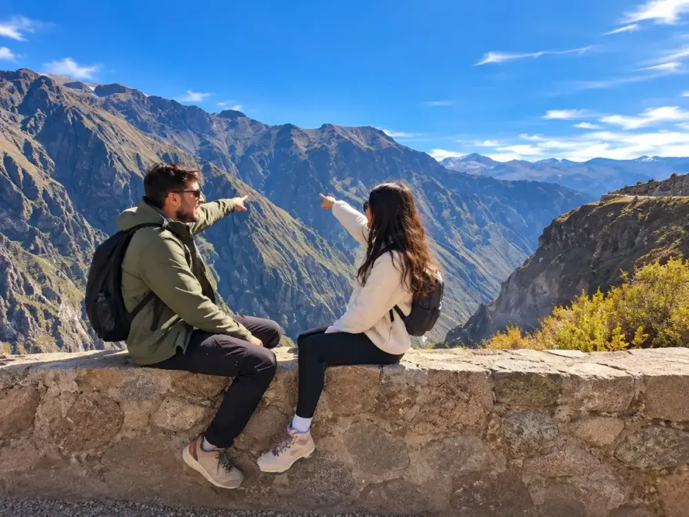 Pareja sentada en muro de piedra apunta hacia el Cañón del Colca en Arequipa
