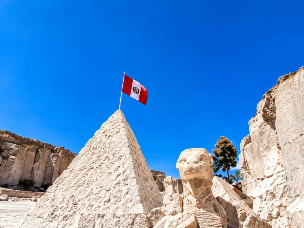 Pirámide y esfinge de sillar con la bandera de Perú bajo un cielo azu