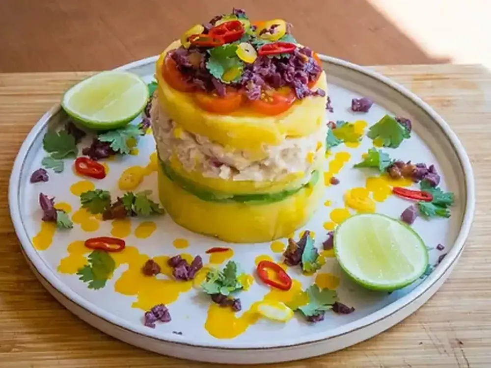 Causa limeña gourmet decorada con aceituna, ají, tomates cherry y hojas de cilantro.