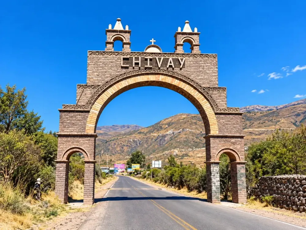 Gran arco de piedra con la palabra Chivay sobre una carretera andina