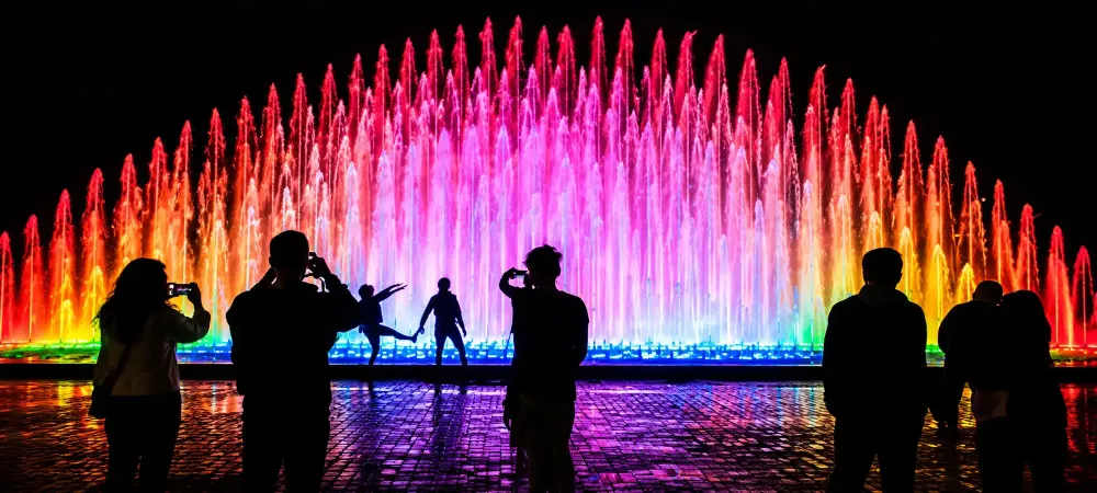 Siluetas de turistas tomando fotos del show en la Fuente de la Fantasía de noche