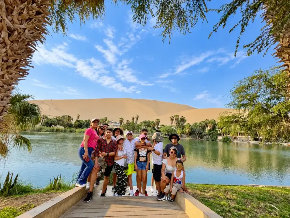 Grupo de turistas junto a la laguna de Huacachina con dunas al fondo en Ica, Perú.