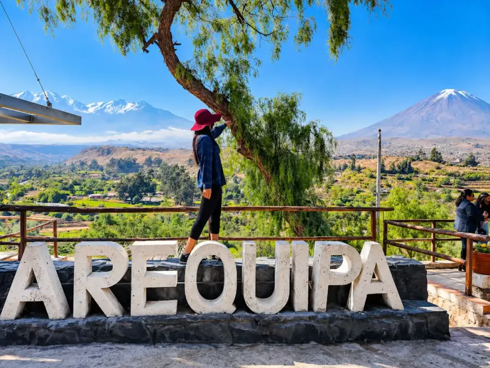 Mujer posa junto al letrero de Arequipa con los volcanes Misti y Chachani detrás