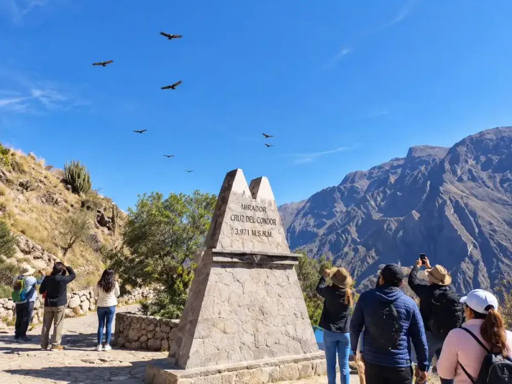 Turistas en el cartel del Mirador Cruz del Cóndor con aves volando en Perú