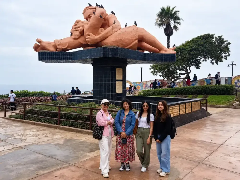 Cuatro mujeres posan sonrientes frente a la escultura El Beso en el Parque del Amor.