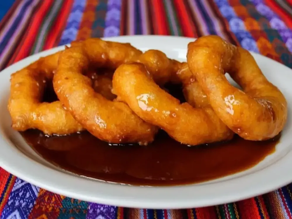 Picarones peruanos bañados en miel de chancaca servidos sobre un plato blanco.