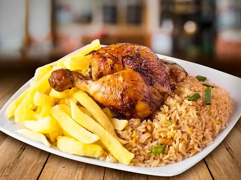 Pollo a la brasa con arroz chaufa y papas fritas servido en un plato cuadrado.