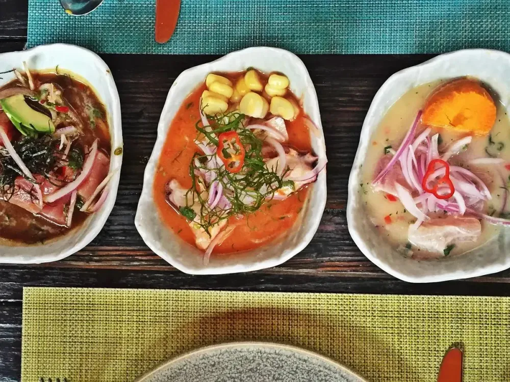 Tres variedades de ceviche peruano servidos en fuentes individuales sobre una mesa.