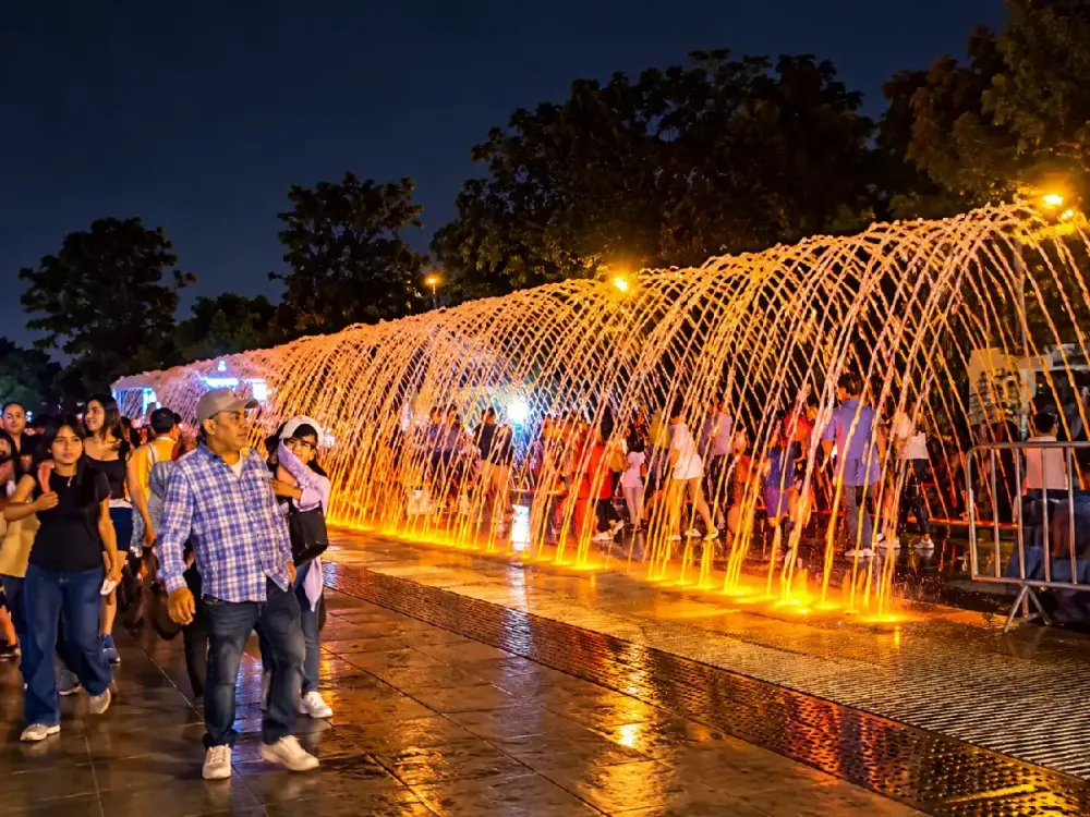 Visitantes cruzando de noche el túnel de agua iluminado de la Fuente de las Sorpresas.