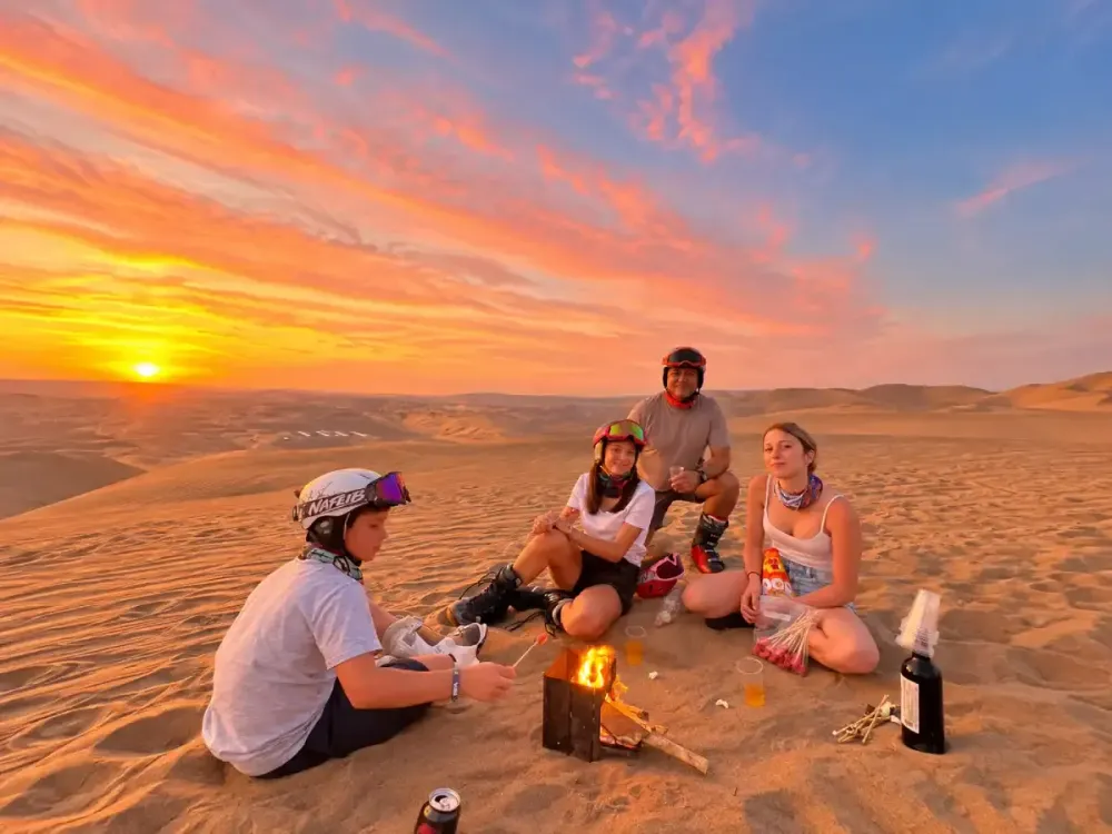 Turistas disfrutando de una fogata al atardecer entre las dunas de Huacachina, Ica, Perú.