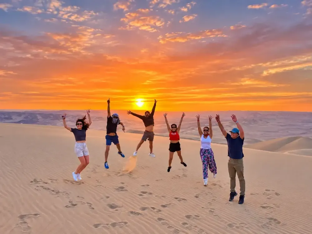 Grupo de turistas saltando sobre las dunas de Huacachina durante el atardecer.