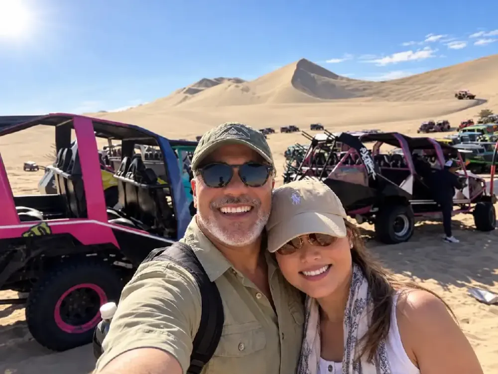 Pareja de turistas tomándose una selfie junto a buggies en las dunas de Huacachina, Ica, Perú.