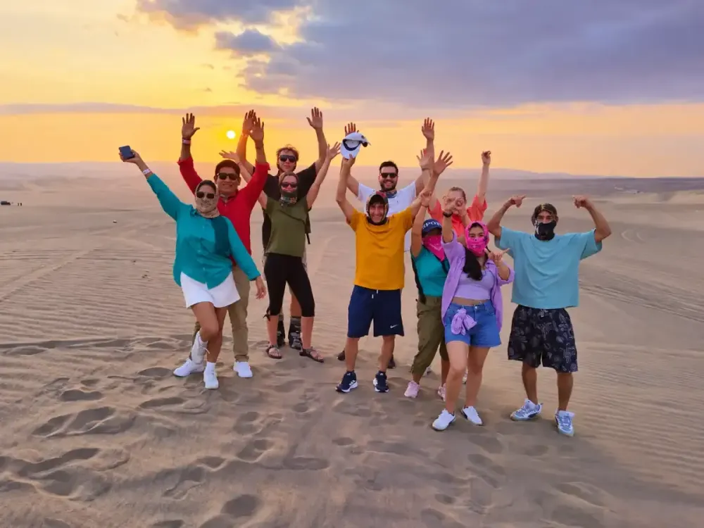Grupo de turistas celebrando al atardecer sobre las dunas de Huacachina, Ica, Perú.