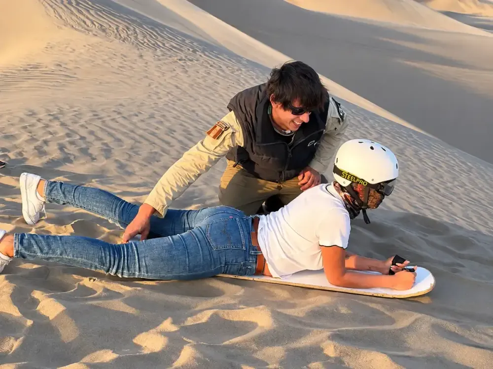 Turista recibiendo instrucciones para practicar sandboarding en las dunas de Huacachina, Ica.
