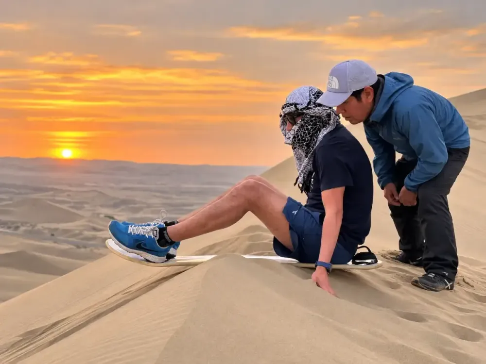 Turista preparándose para hacer sandboarding en las dunas de Huacachina al atardecer.