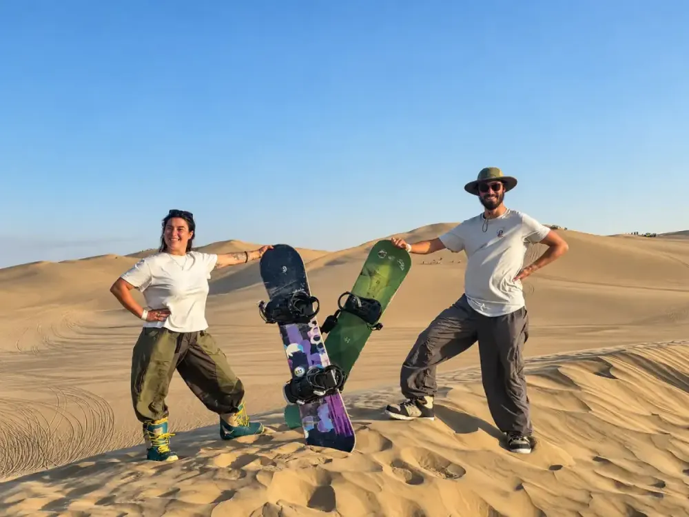Pareja de turistas con tablas de sandboarding en las dunas de Huacachina, Ica, Perú.