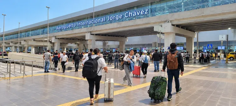 Pasajeros caminando con equipaje de noche fuera del Aeropuerto Jorge Chávez de Lima.
