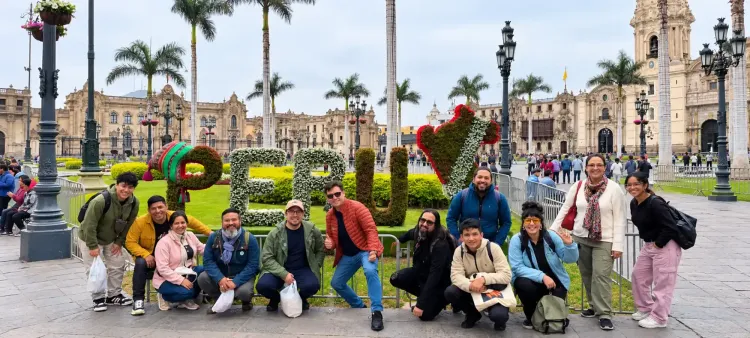 Un grupo de turistas posa sonriente junto a un gran letrero floral que dice PERÚ en la Plaza Mayor de Lima.